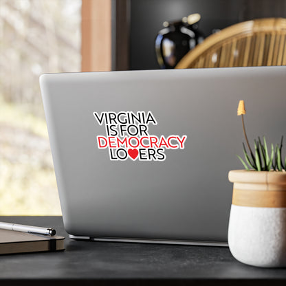Laptop with a sticker reading 'Virginia is for Democracy Lovers' on a desk with a plant and pen.