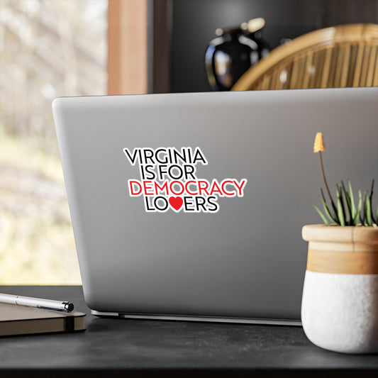 Laptop with a sticker reading 'Virginia is for Democracy Lovers' on a desk with a plant and pen.