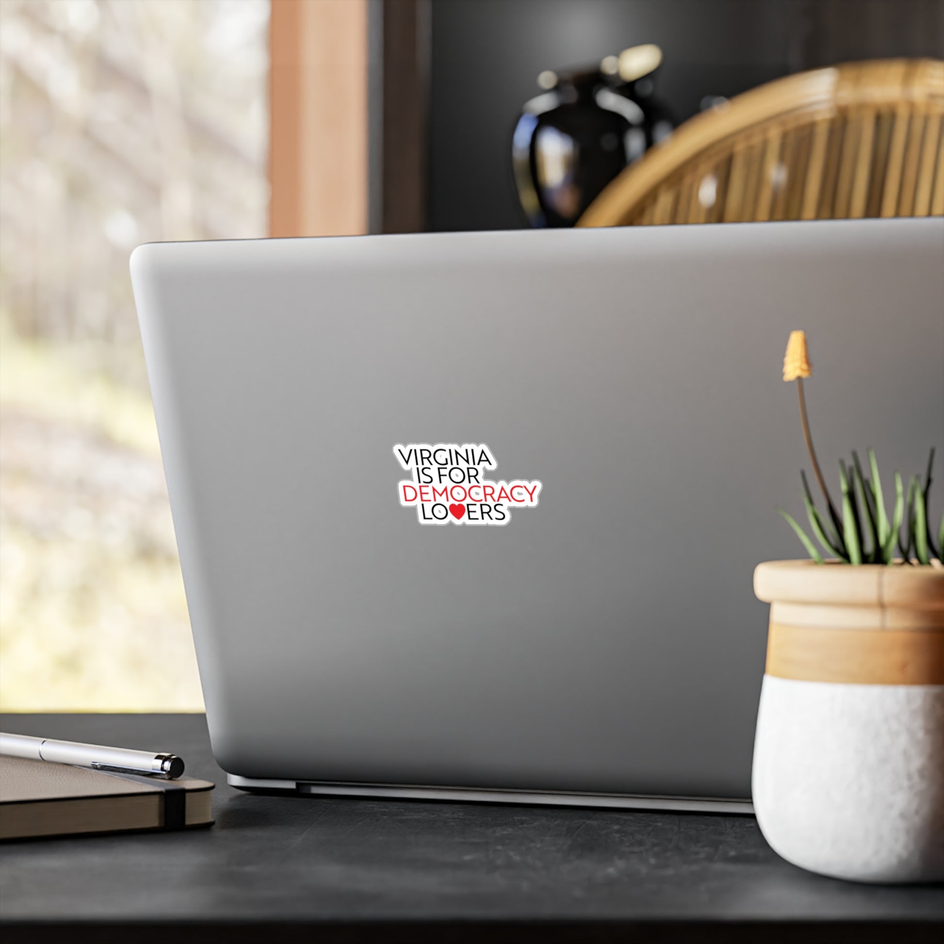 Laptop with a sticker on a desk with a plant and pen