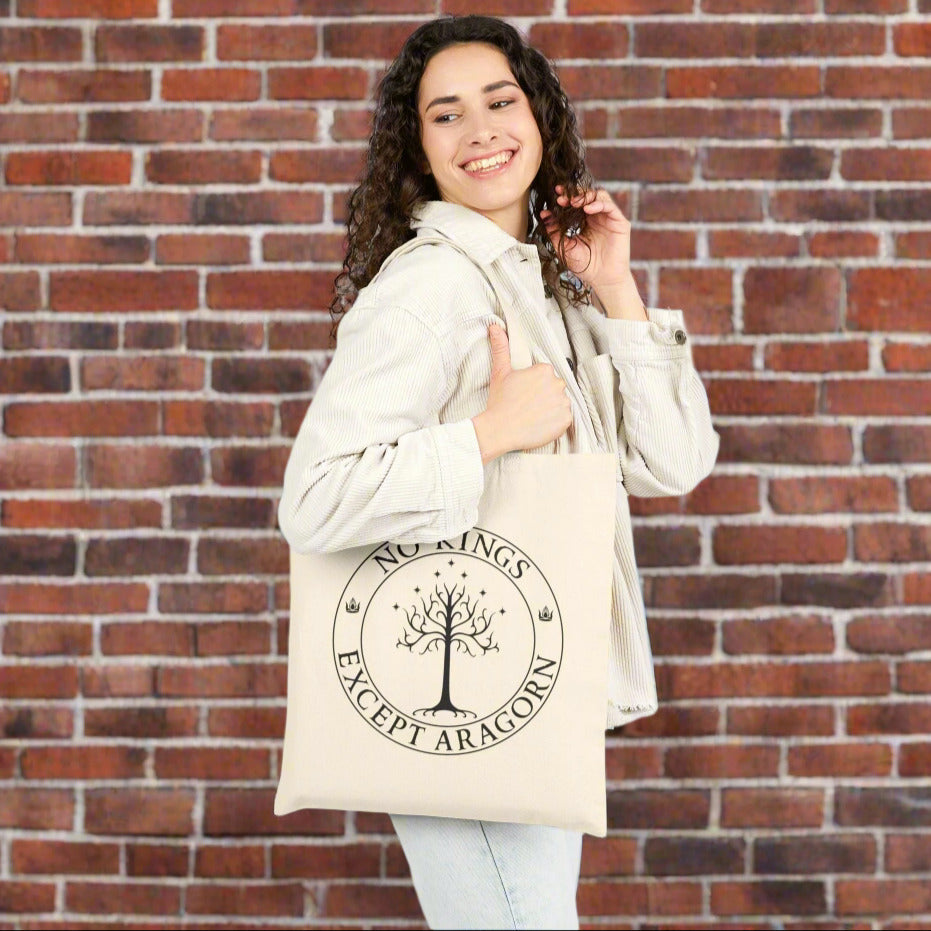 A woman carrying a tan tote back with the text "No kings except Aragorn" and a graphic f a tree with seven stars above it and two crowns of the king of Gondor.