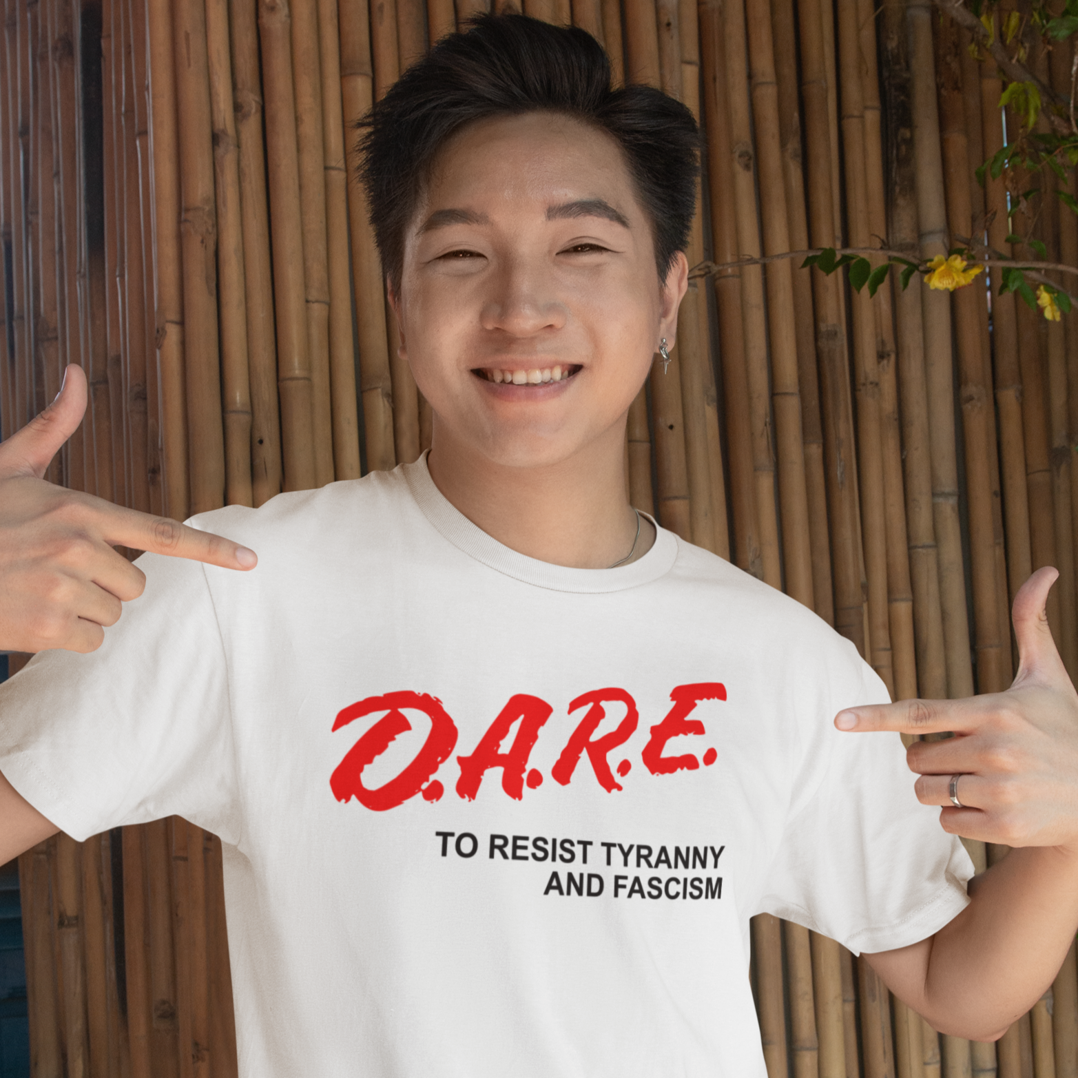 Person wearing a white t-shirt with red and black text, pointing to the text outdoors.