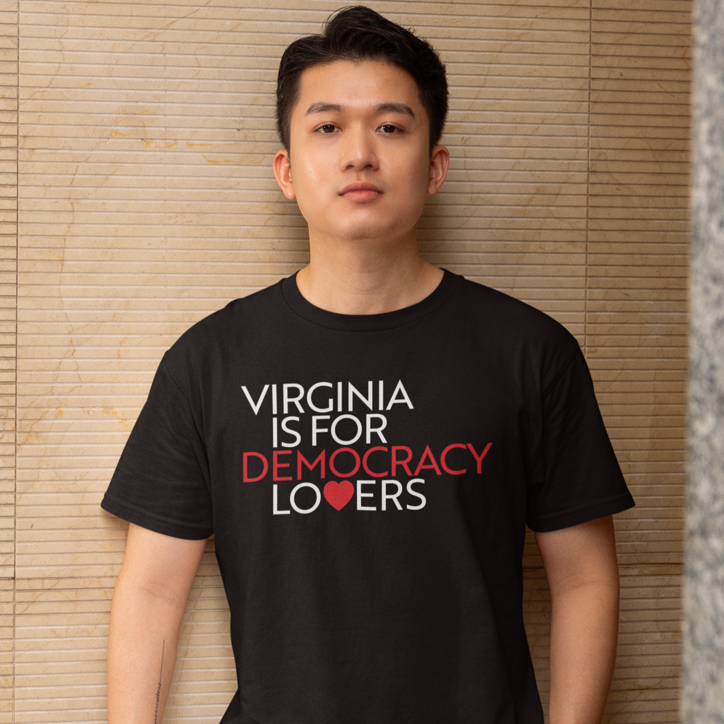Person wearing a black t-shirt with 'Virginia is for Democracy Lovers' text, standing against a textured wall.