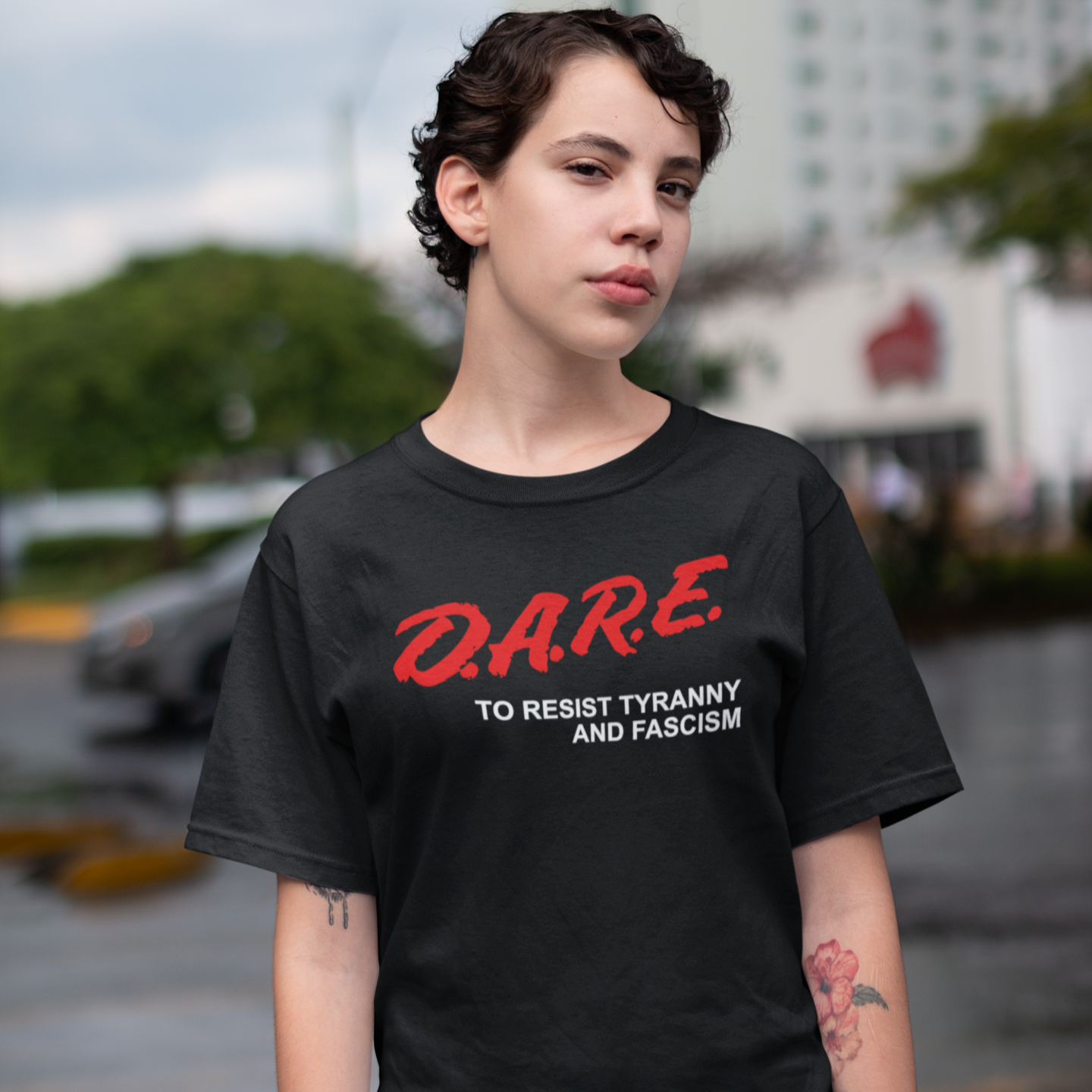 Person wearing a black t-shirt with 'D.A.R.E. to resist tyranny and fascism' text outdoors.